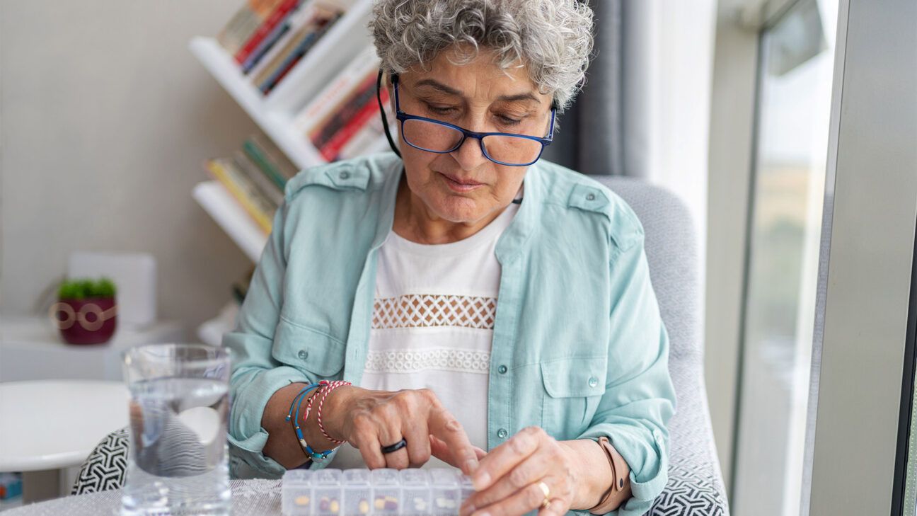 Woman with glasses looks at pills in a pill case. 
