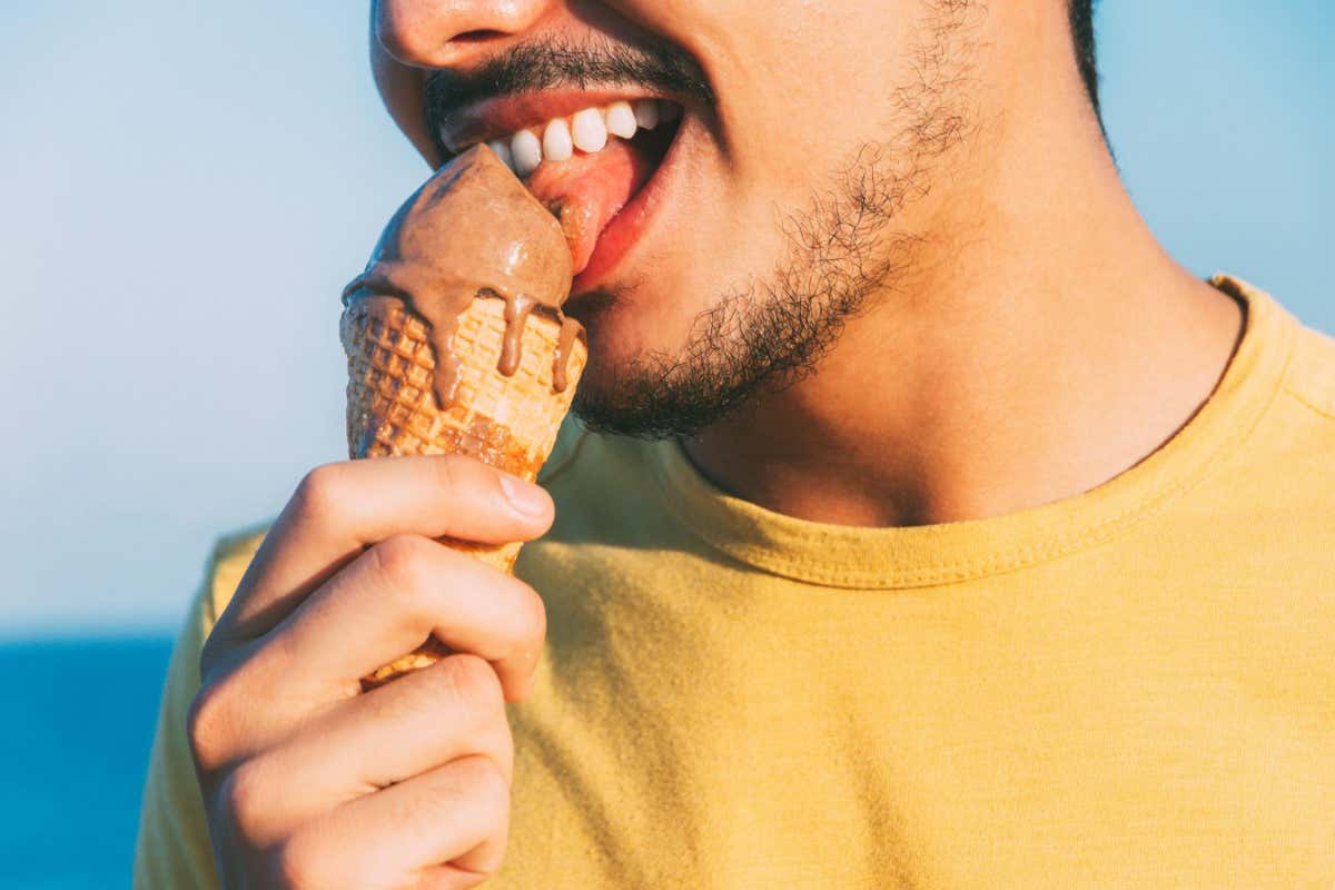 2C6AJB8 young man in yellow licks his chocolate ice cream