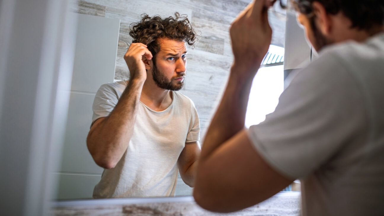 A man examining his hair in a mirror.